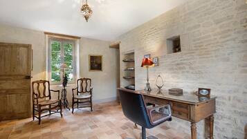 A room with a desk, two chairs, a chandelier, and a window with a view of greenery.