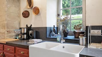 A kitchen with a large white sink, wooden cabinets, and a window with a view of greenery.