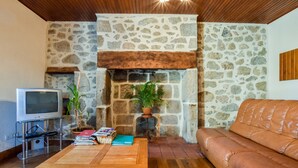Uma sala de estar com lareira de pedra, sofá de couro, mesa de centro de madeira e televisão.