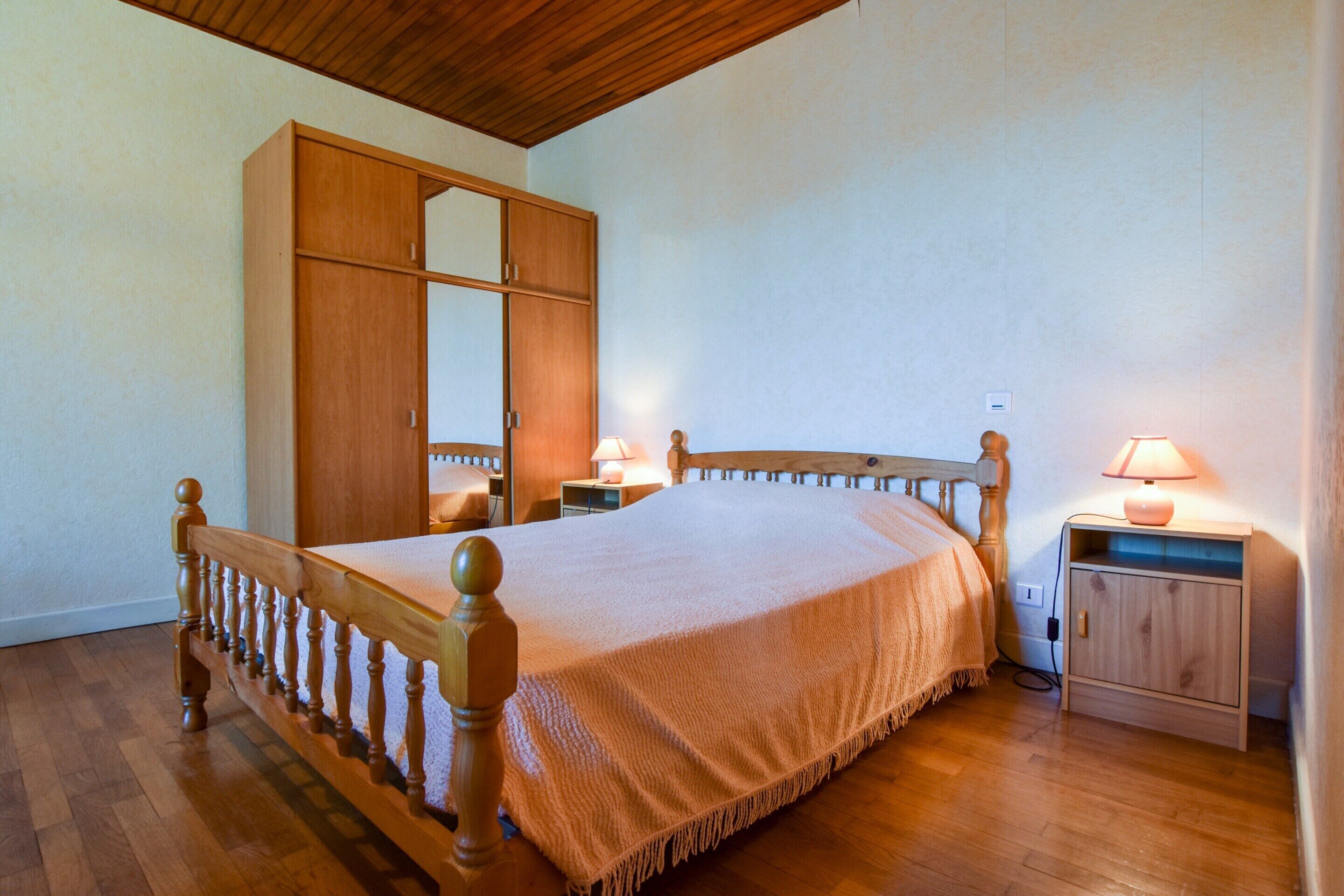 Un dormitorio con una cama de madera, un armario, una mesita de noche y una lámpara.