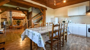 Uma sala de jantar com uma mesa posta para seis, cadeiras de madeira, uma escada e uma cozinha com armários e eletrodomésticos brancos.