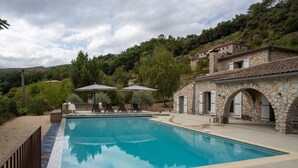 A swimming pool with stone architecture, outdoor seating, and a hillside backdrop. - Villa Near Les Vans With Private Pool (Les Salelles)