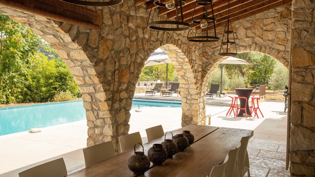 A stone archway leading to a pool area with outdoor seating and a wooden table with decorative vases. - Villa Near Les Vans With Private Pool (Les Salelles)