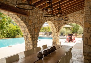 Un arc en pierre mène à un espace piscine agrémenté d’un coin salon extérieur et d’une table en bois ornée de vases décoratifs.