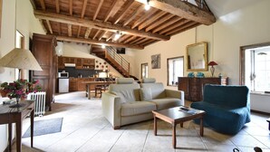 Ein großzügiger Wohnbereich mit Sofa, Sessel und Couchtisch, im Hintergrund eine Küche und eine Treppe, die zu einer oberen Ebene führt.