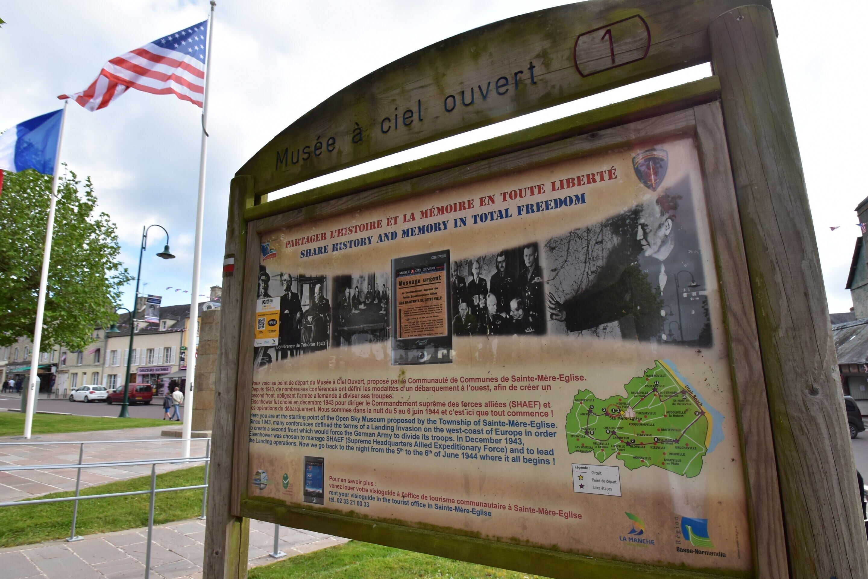 A historical marker with text and a map, featuring an American flag and a blue flag.