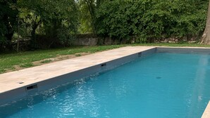 Ein rechteckiger Swimmingpool mit klarem, blauem Wasser, umgeben von einer Steinmauer und Grünpflanzen.