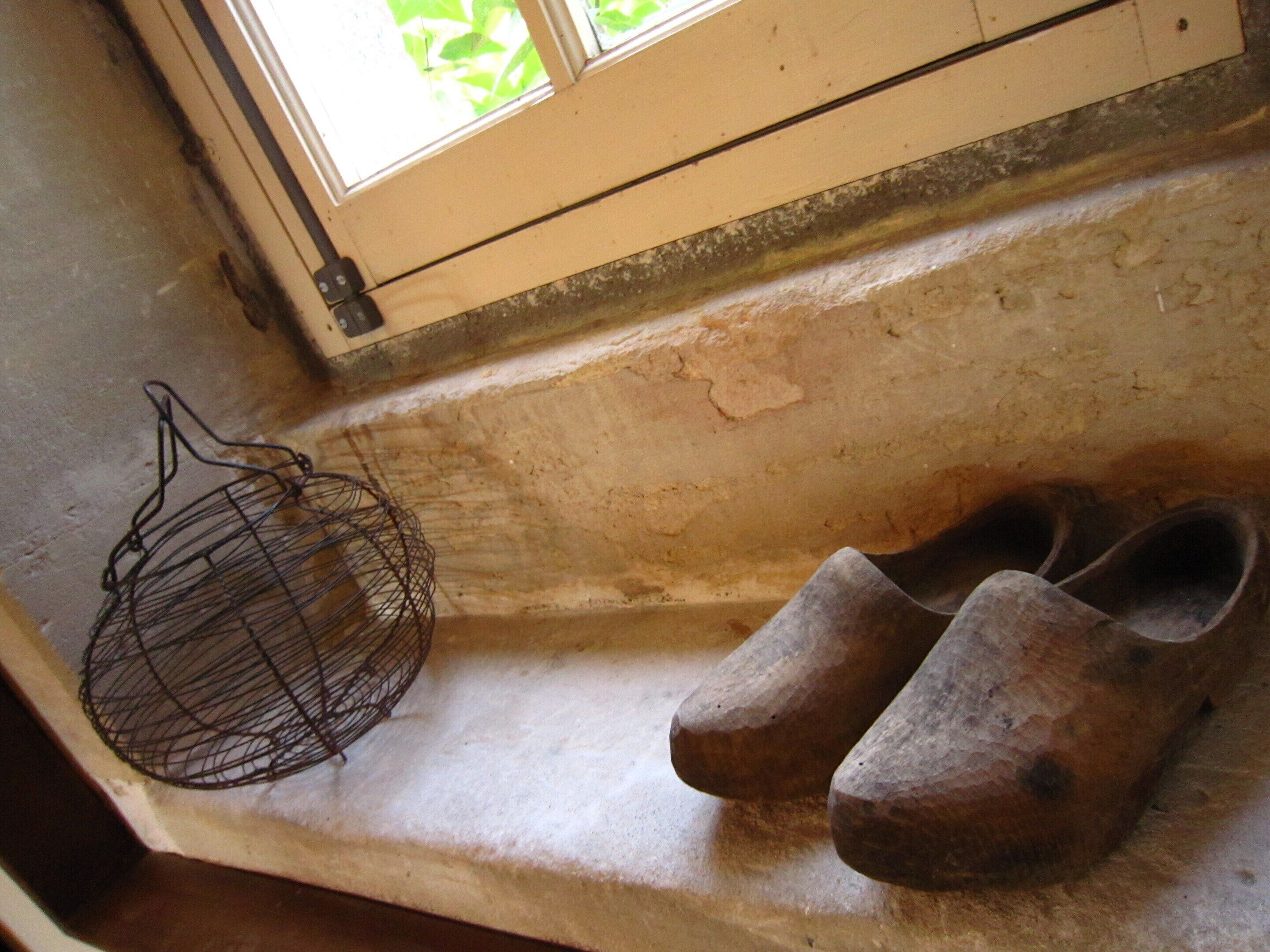 A wooden bench with a metal basket and a pair of wooden shoes.