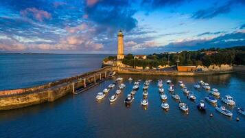 A coastal scene with a lighthouse, a harbor with numerous boats, and a stone wall.