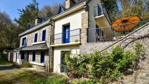 A two-story stone building with a balcony, a staircase with an umbrella, and a door with a blue frame. - Charming Brittany Hideaway (Yvias)
