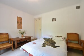 Een slaapkamer met een bed, twee houten stoelen, een tafeltje met een vaas en een deur.