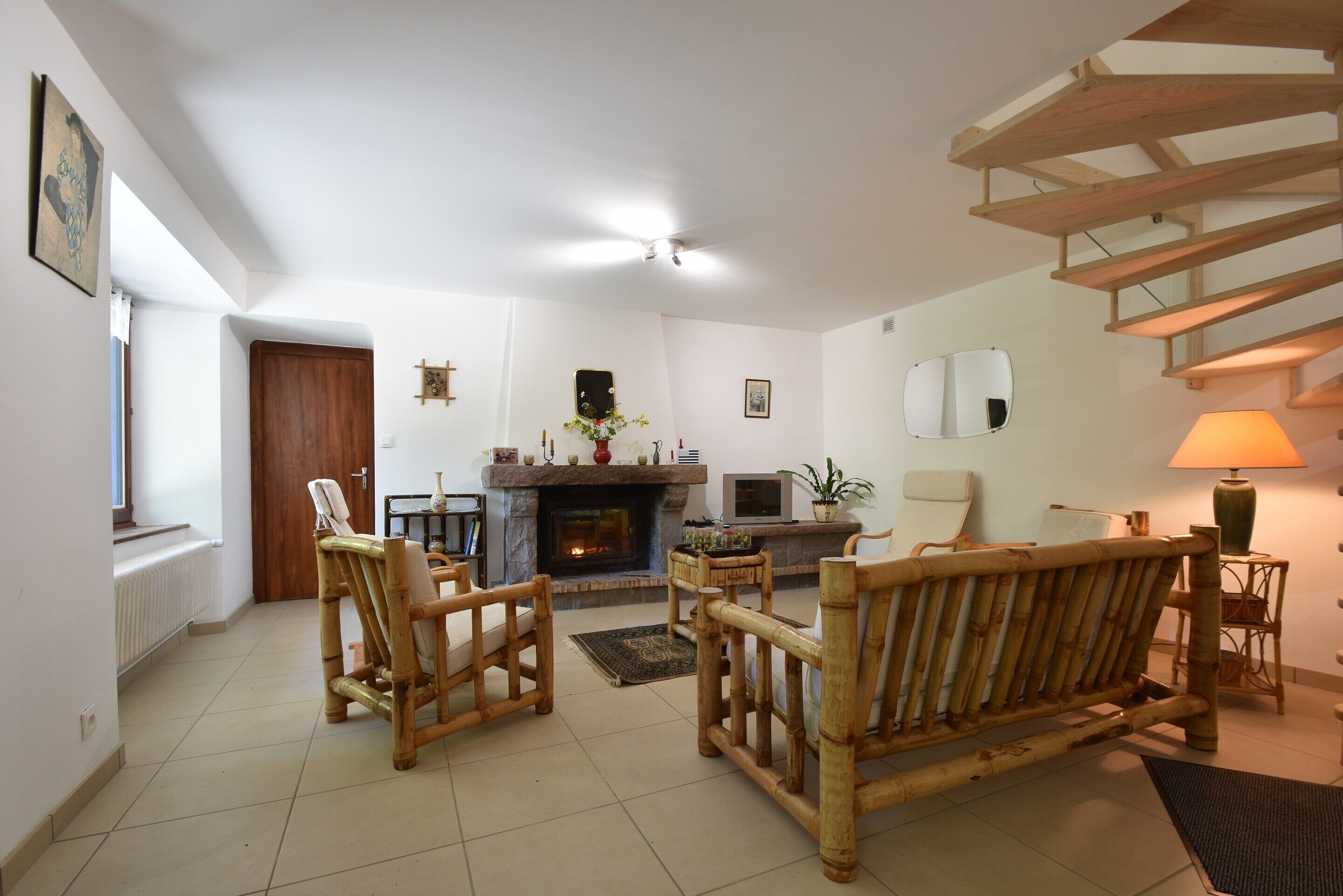 A living room with a fireplace, wooden furniture, a staircase, and a view of the outside.