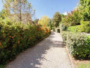 A gravel path flanked by dense shrubbery and a building with a pointed roof. - Family Home in Carsac-aillac (Carsac-Aillac)