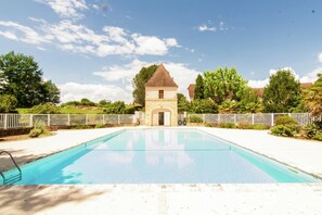 Une piscine avec un petit bâtiment en arrière-plan, entourée de verdure et d’une clôture blanche.