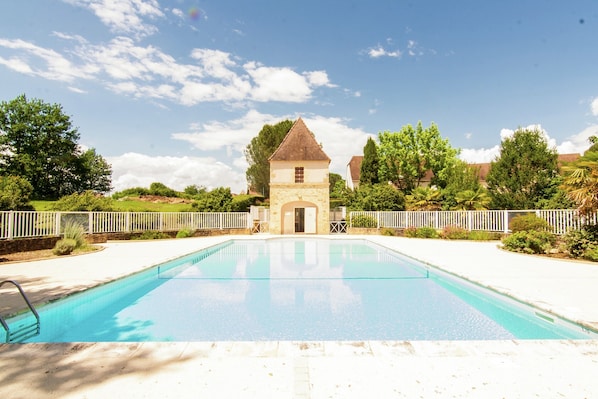 A swimming pool with a small building in the background, surrounded by greenery and a white fence. - Family Home in Carsac-aillac (Carsac-Aillac)