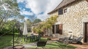 Ein Steinhaus mit einer Terrasse, ausgestattet mit Gartenmöbeln und einer Schaukel.