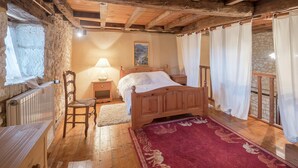 Ein rustikales Schlafzimmer mit einem hölzernen Bett, einem Nachttisch, einem Sessel, einem roten Teppich und Steinwänden.