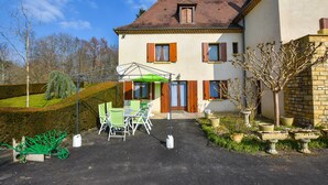A two-story house with a patio area featuring a table and chairs, a green umbrella, and potted plants. - House in Perigord Near Medieval Villages (Prats-du-Perigord)