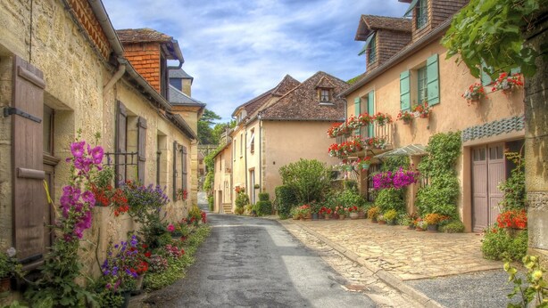 A narrow cobblestone street flanked by historic buildings with flower boxes and greenery. - House in Perigord Near Medieval Villages (Prats-du-Perigord)