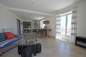 A modern living room with a sofa, a glass-top dining table, and a kitchen in the background. - Peaceful Poolside Escape (Montouliers)