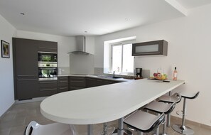 A modern kitchen with a central island, bar stools, and a window providing natural light. - Peaceful Poolside Escape (Montouliers)