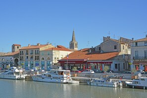 A marina with boats docked, buildings with commercial establishments, and a prominent church spire. - Peaceful Poolside Escape (Montouliers)