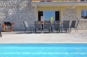 Un espace aménagé au bord de la piscine, avec une table et des chaises, un barbecue et un mur en pierre.