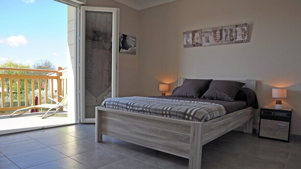 A bedroom with a bed, two bedside lamps, a nightstand, a sliding glass door to a balcony, and a wall-mounted artwork. - Luxury Villa With Private Pool (Saint-Victor-de-Malcap)