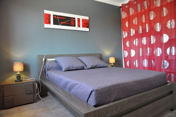A bedroom with a bed, two bedside tables with lamps, a wall-mounted artwork, and a red curtain with circular patterns. - Luxury Villa With Private Pool (Saint-Victor-de-Malcap)