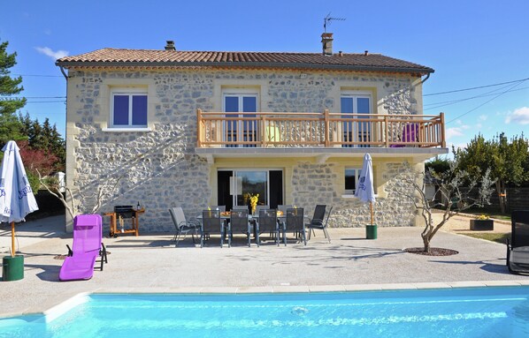 Un bâtiment en pierre de deux étages, doté d’un balcon, d’une piscine et d’un espace extérieur aménagé pour s’asseoir.