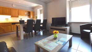 A modern living room with a dining area, a TV, and a kitchen in the background. - Lovely Modern Apartment, Near the Mosel, Shops and Restaurants (Zell (Mosel))
