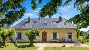 Une maison à deux étages avec une porte rouge, un petit jardin et un chemin de gravier menant à l’entrée.