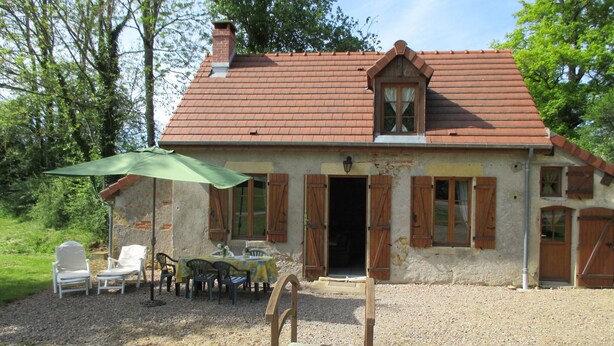 Een landelijk huis met een rode dakbedekking van tegels, houten luiken en een grindpad.