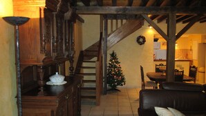 Een gezellige zithoek met een houten trap, een kerstboom, een eettafel en een leren bank.
