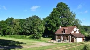 Een rustiek huis met een schuin dak, een schotelantenne en een klein terras met een tafel en stoelen.