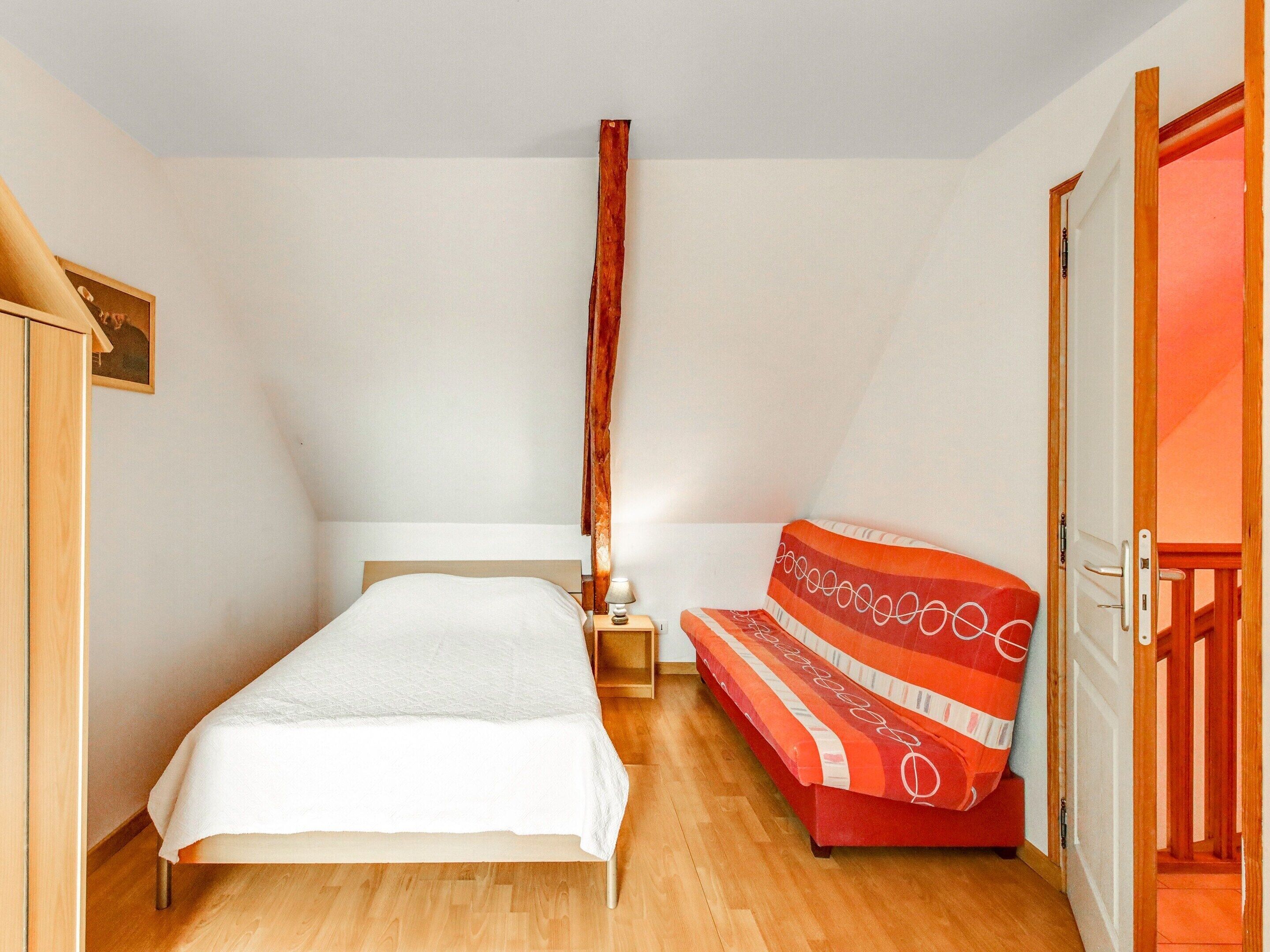 Un dormitorio con una cama, una mesita de noche, un sofá a rayas rojas y una puerta de madera.