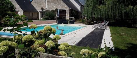 Una piscina con muelle de madera y sillas de descanso, rodeada de follaje y edificios de piedra.