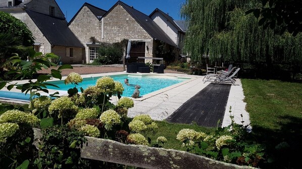 A swimming pool with a wooden deck and lounge chairs, surrounded by greenery and stone buildings. - Riverside Hideaway in Cinais (Cinais)