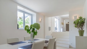 A modern dining area with a white table, chairs, and a vase with green plants. There are windows providing natural light and a view of the outside. - Retreat in Beaumont-en-veron (Beaumont-en-Veron)