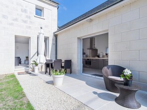 Una casa moderna con patio, arredi da esterno e una cucina visibile attraverso un'apertura.