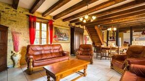 A rustic interior with wooden beams, leather sofas, a dining area, and a staircase. - Blanquefort Hill Retreat (Blanquefort-sur-Briolance)