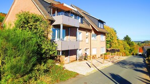 Un edificio residenziale a due piani con tetto spiovente, un balcone al piano superiore e un vialetto sterrato.