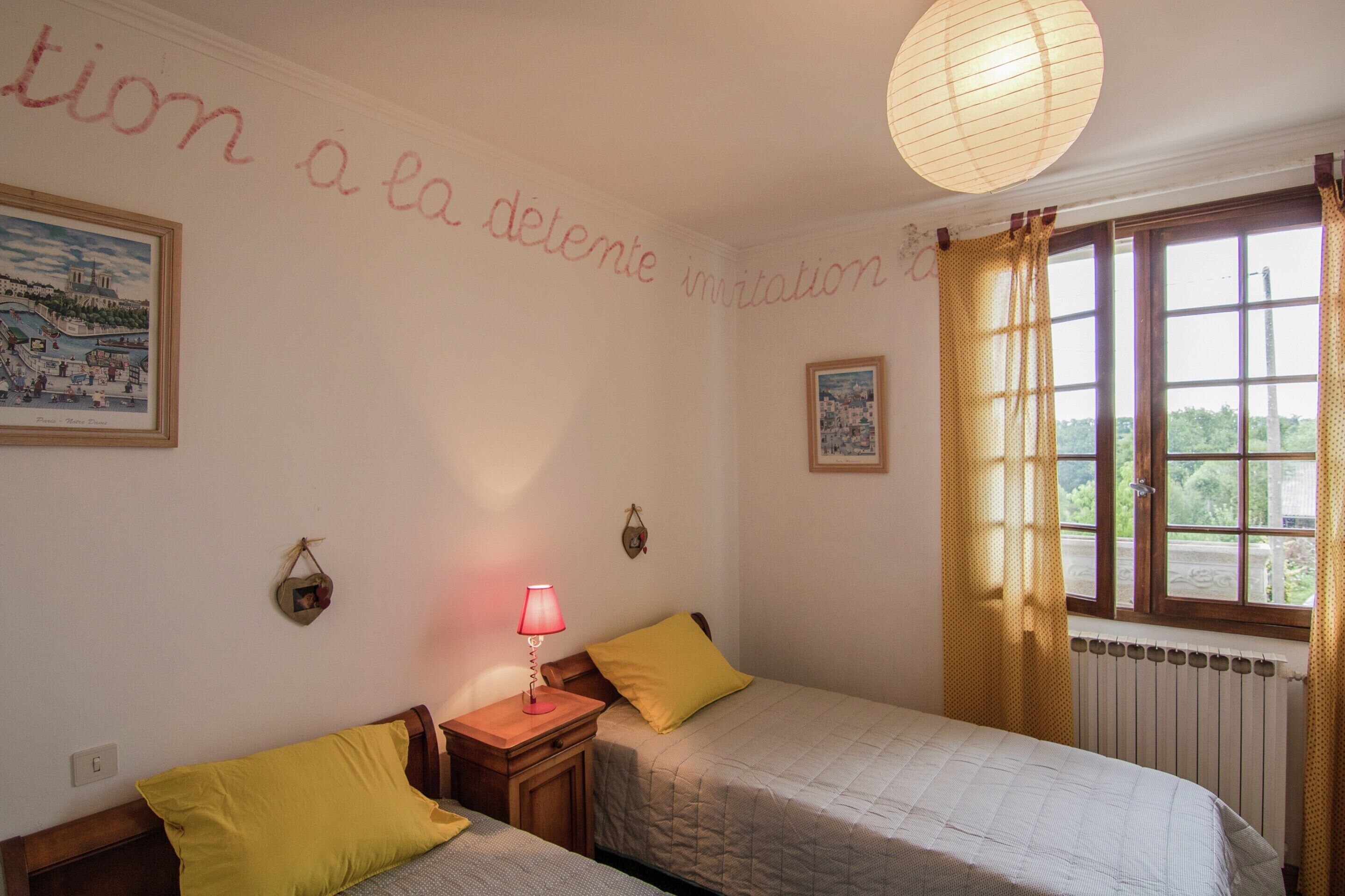 Une chambre avec deux lits, une table de chevet avec une lampe, une fenêtre avec des rideaux et des éléments de décoration murale.