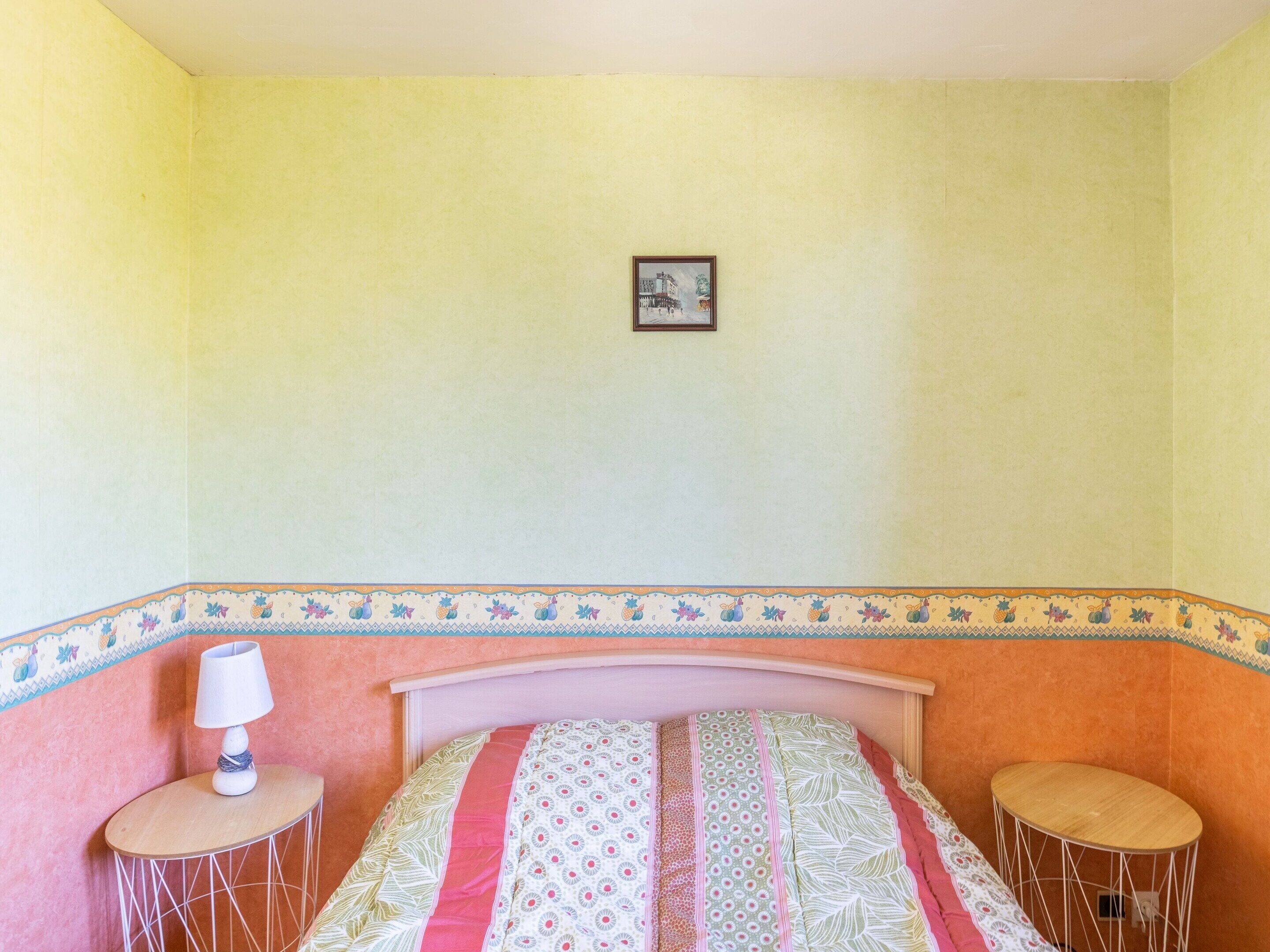A room with a bed, a small table with a lamp, and a picture on the wall.