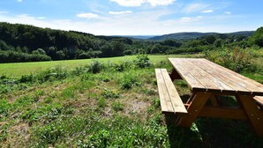 Une table de pique-nique en bois, installée dans un champ verdoyant, d’où l’on peut admirer des collines ondoyantes et un ciel dégagé.