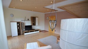 Ein geräumiges Zimmer mit Holzbalkendecke, einem Bett, einem Fernseher und einem großen, weißen zylindrischen Objekt.