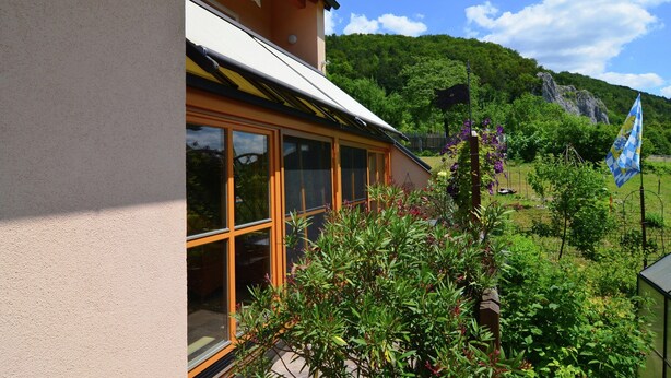 Ein Gebäude mit großen Fenstern und einem Balkon mit Blick auf einen Garten mit verschiedenen Pflanzen und einer Flagge.