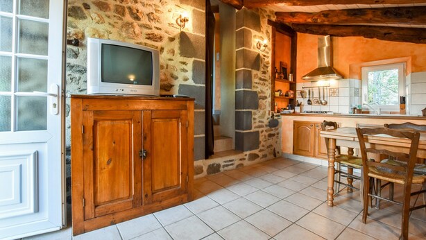A rustic kitchen with stone walls, wooden cabinets, a tiled floor, and a wooden dining table with chairs. - Saint-beauzire Holiday Home Near Pauillac Castle (Saint-Beauzire)