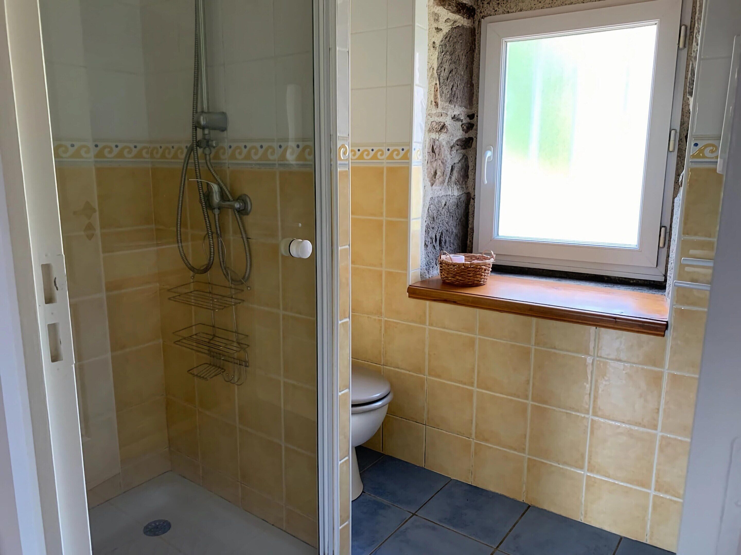 A bathroom with a shower, toilet, and a window with a basket on the sill.