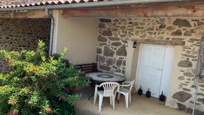 A stone building with a tiled roof, a white door, and a small patio area with a table and chairs. - Saint-beauzire Holiday Home Near Pauillac Castle (Saint-Beauzire)